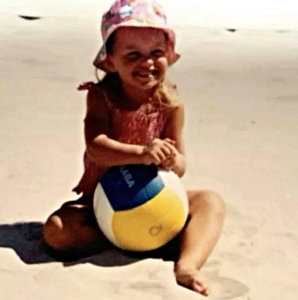 Little girl on the beach smiling playing volleyball. 